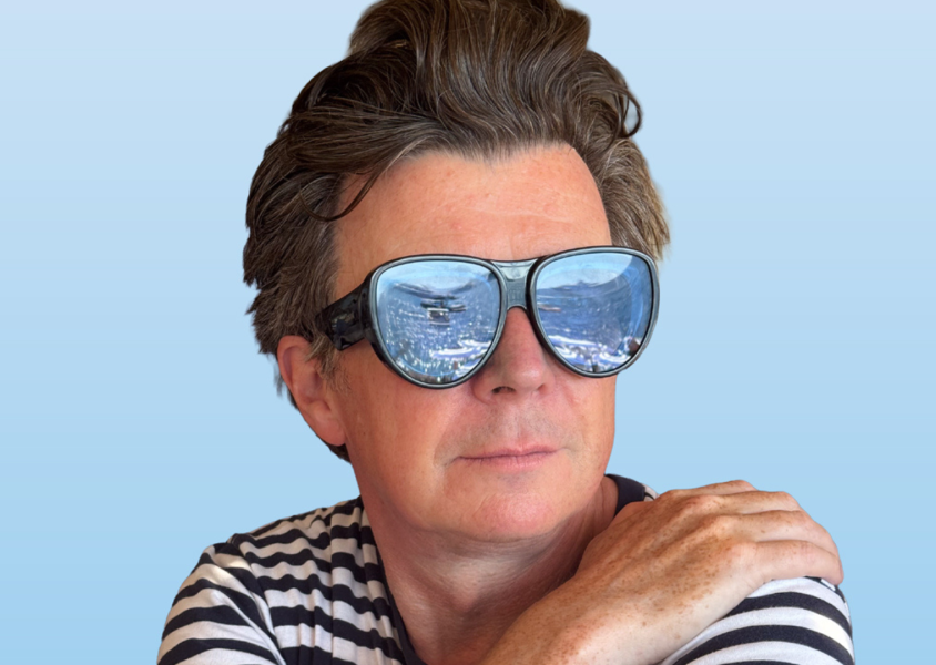 Musician Rick Astley wearing sunglasses which reflect a crowd.x